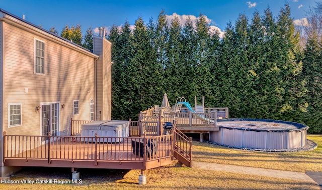 exterior space featuring a wooden deck, a covered pool, a chimney, and a hot tub