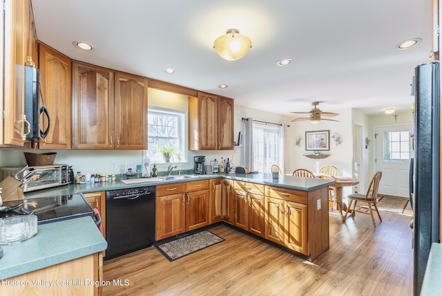 kitchen with brown cabinetry, a peninsula, black appliances, light wood-style floors, and a wealth of natural light