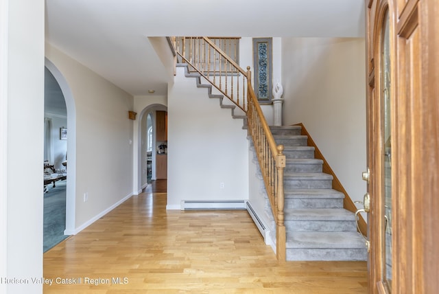 foyer featuring light wood-style flooring, stairway, arched walkways, baseboards, and baseboard heating