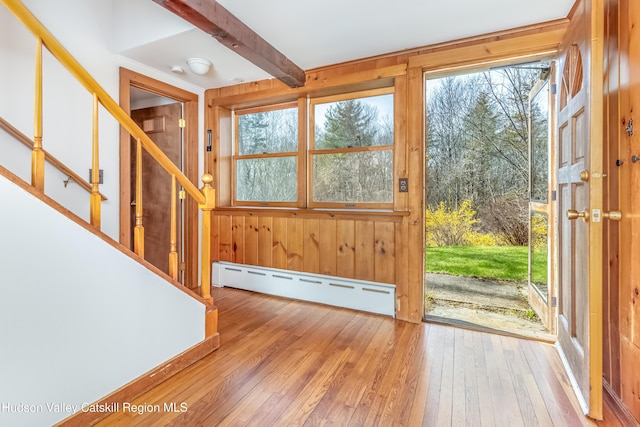 foyer featuring baseboard heating, wood-type flooring, wood walls, and stairway