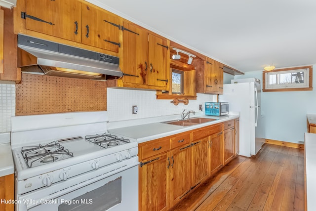 kitchen with under cabinet range hood, light countertops, a sink, white appliances, and light wood-style floors