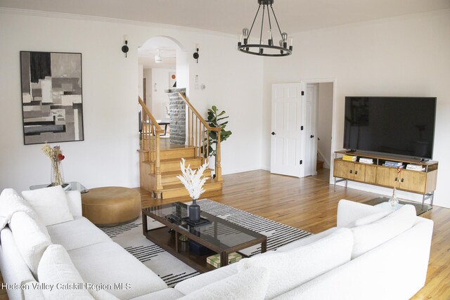 living area featuring arched walkways, an inviting chandelier, wood finished floors, and stairway