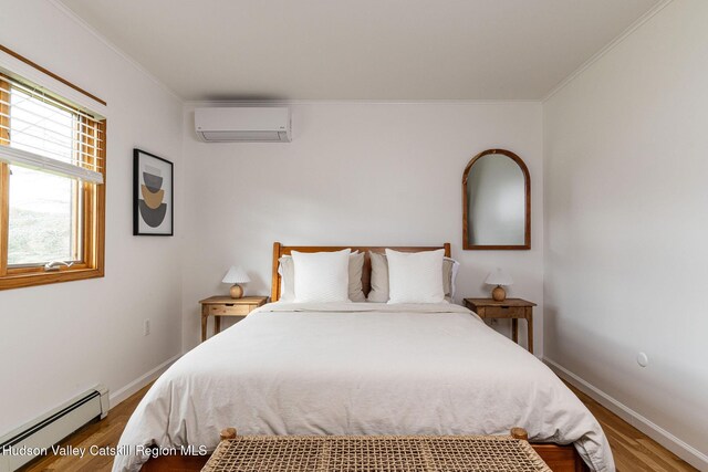 bedroom with baseboard heating, baseboards, wood finished floors, a wall mounted AC, and ornamental molding