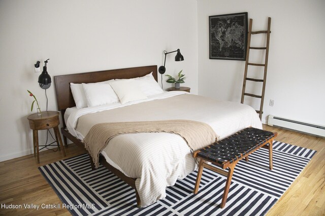 bedroom with a baseboard heating unit and wood finished floors