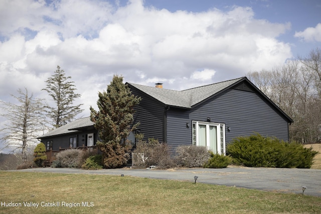 view of side of home with a shingled roof, a yard, and a chimney