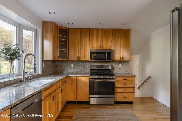 kitchen featuring decorative backsplash, appliances with stainless steel finishes, light stone countertops, wood finished floors, and a sink