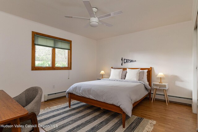 bedroom featuring a ceiling fan, baseboard heating, a baseboard heating unit, and wood finished floors