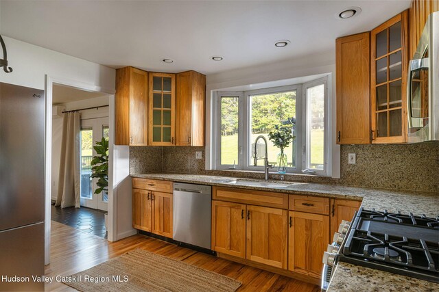 kitchen featuring stainless steel appliances, brown cabinetry, a sink, and light wood-style floors