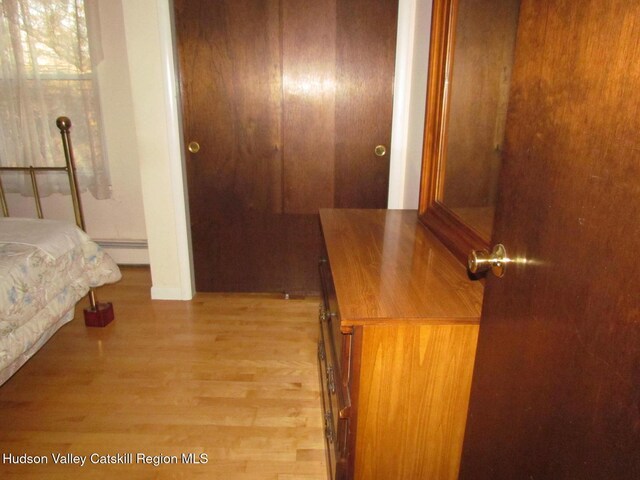 bedroom with a closet, light hardwood / wood-style flooring, and a baseboard heating unit