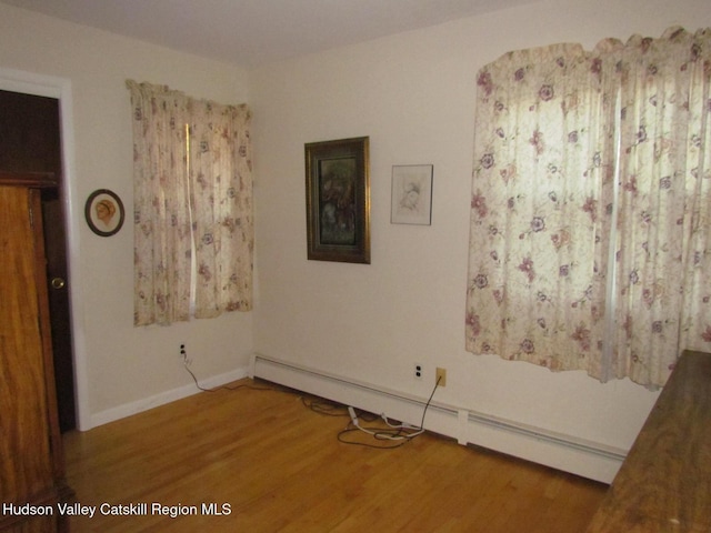 unfurnished room featuring baseboard heating and wood-type flooring