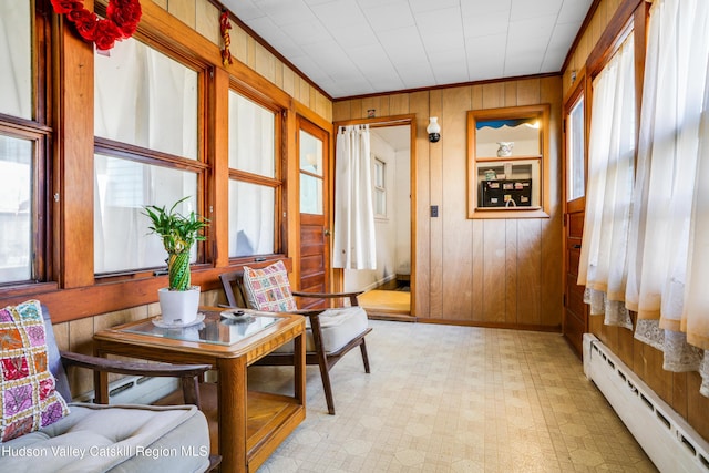 living area featuring ornamental molding, wooden walls, and a baseboard heating unit