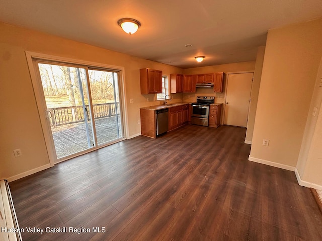 kitchen with dark wood-style flooring, stainless steel appliances, brown cabinetry, under cabinet range hood, and baseboards