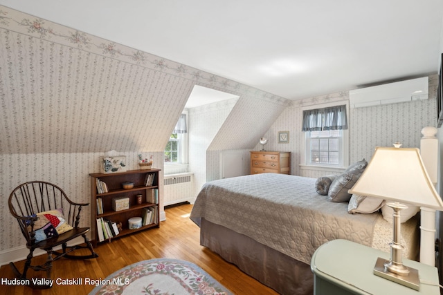 242 N Manor Ave, Kingston, NY 12401 - bedroom with radiator heating unit, wallpapered walls, wood finished floors, an AC wall unit, and vaulted ceiling
