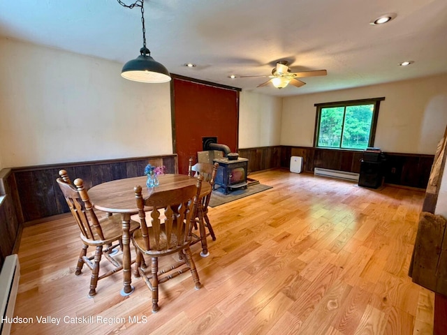 65 Bluebird Ln, Andes, NY 13731 - dining room featuring a wood stove, baseboard heating, a wainscoted wall, ceiling fan, and light wood-type flooring