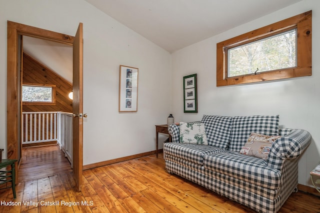 living area featuring lofted ceiling, wooden walls, and light hardwood / wood-style flooring