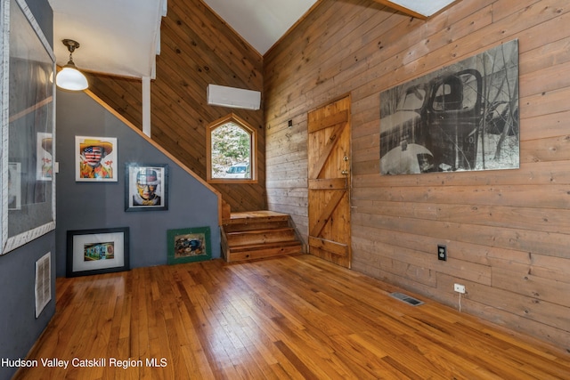 unfurnished living room featuring wood-type flooring, a barn door, high vaulted ceiling, and wooden walls