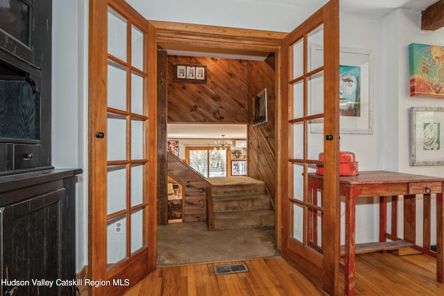 hallway featuring french doors, hardwood / wood-style flooring, wooden walls, and beam ceiling