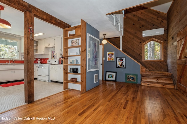 living room with a wall mounted air conditioner, hardwood / wood-style floors, sink, and wood walls