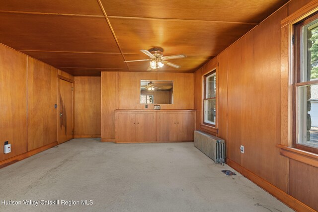 spare room featuring radiator, ceiling fan, wood walls, light colored carpet, and wood ceiling