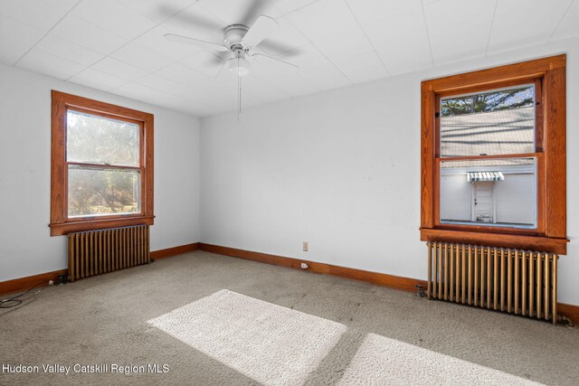 carpeted empty room featuring ceiling fan and radiator