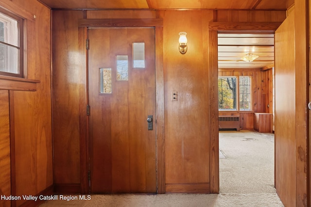 hallway featuring radiator, wood walls, light carpet, and wooden ceiling