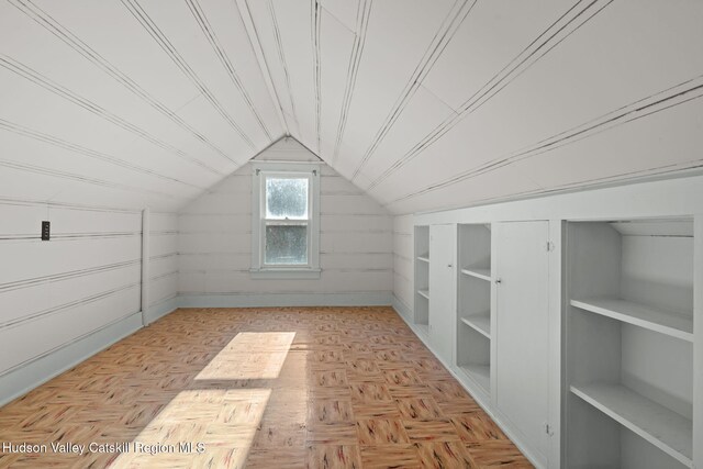 additional living space featuring built in shelves, wood walls, light parquet floors, and vaulted ceiling