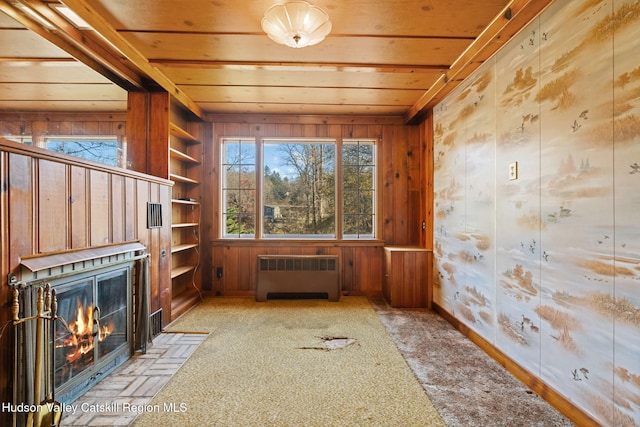 interior space featuring wooden walls, light colored carpet, radiator, and a healthy amount of sunlight