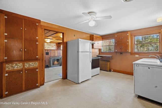 kitchen with white refrigerator, sink, wooden walls, ceiling fan, and range