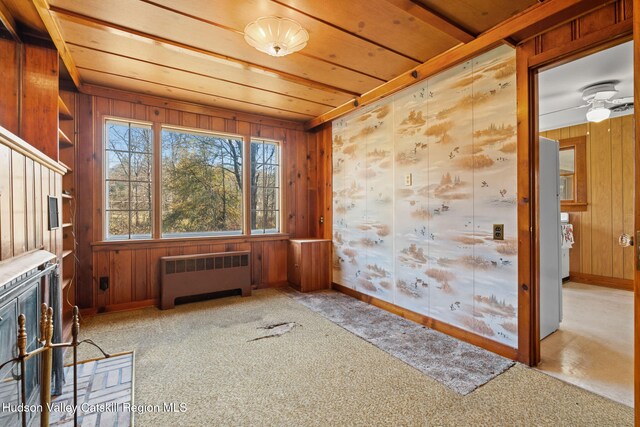 interior space featuring light carpet, radiator heating unit, and wood walls