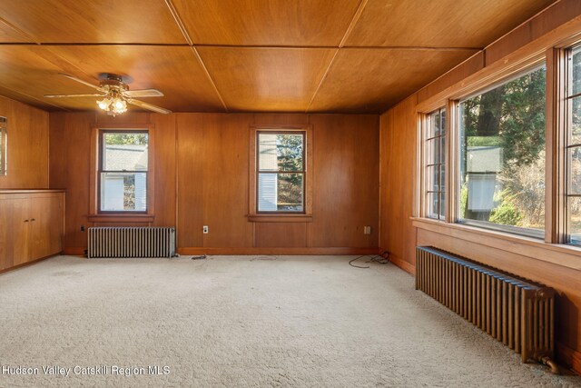 carpeted spare room with wood walls, radiator heating unit, and a healthy amount of sunlight