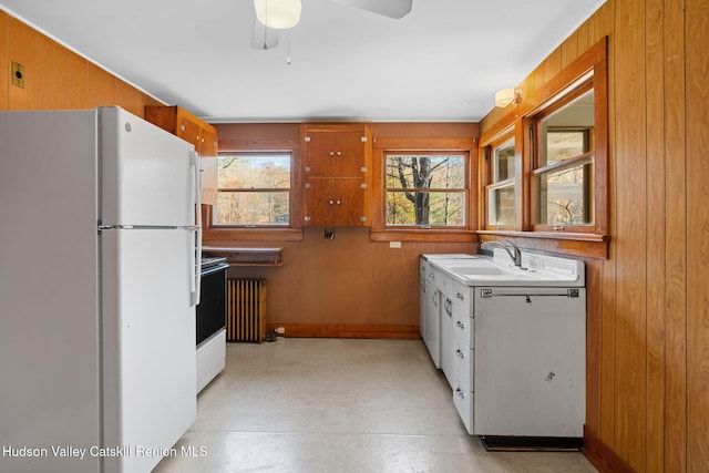 kitchen with ceiling fan, sink, radiator heating unit, white appliances, and wooden walls