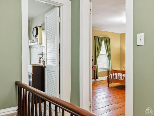 corridor featuring hardwood / wood-style flooring, an upstairs landing, and baseboards