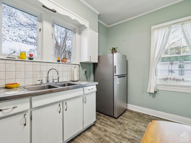 kitchen featuring freestanding refrigerator, a sink, light wood-type flooring, crown molding, and decorative backsplash