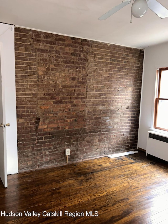 unfurnished room with ceiling fan, brick wall, hardwood / wood-style flooring, and radiator