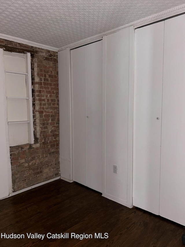 unfurnished bedroom with dark wood-style floors and brick wall