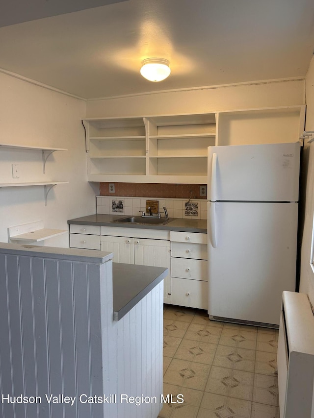 kitchen featuring a sink, white cabinets, freestanding refrigerator, open shelves, and dark countertops