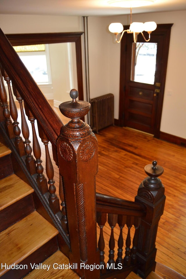 stairs with wood-type flooring, radiator, and a notable chandelier