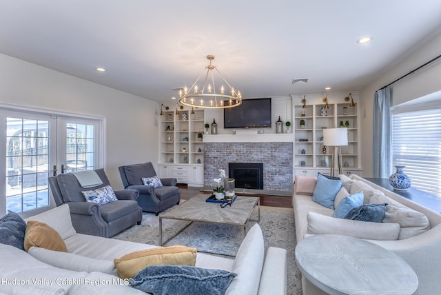 living room featuring a notable chandelier, recessed lighting, visible vents, a brick fireplace, and wood finished floors