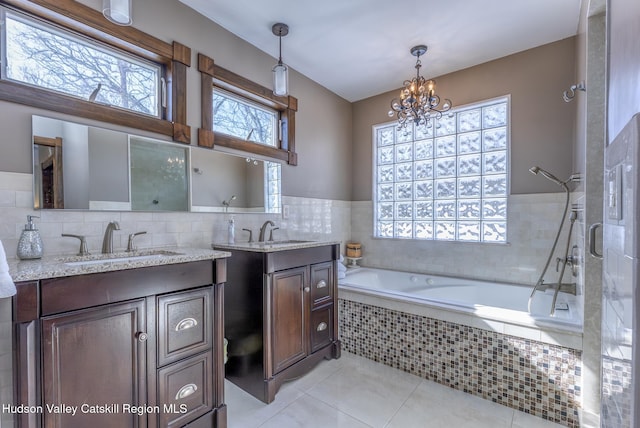 bathroom featuring tile patterned flooring, tiled bath, two vanities, and a sink