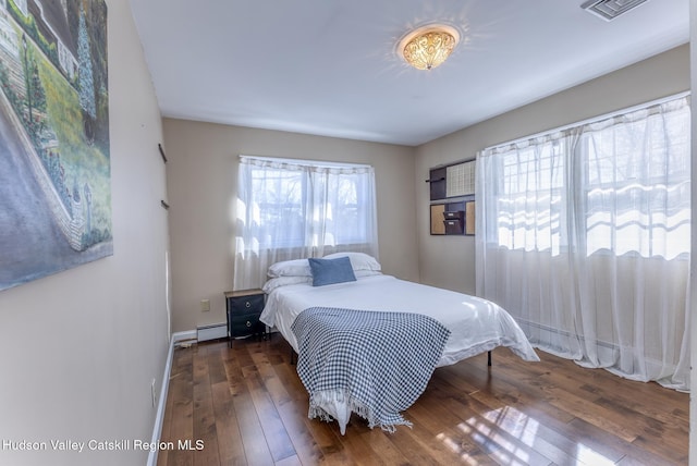 bedroom featuring dark wood-style floors, baseboards, visible vents, and a baseboard heating unit