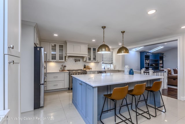 kitchen featuring a center island, hanging light fixtures, appliances with stainless steel finishes, glass insert cabinets, and light stone countertops