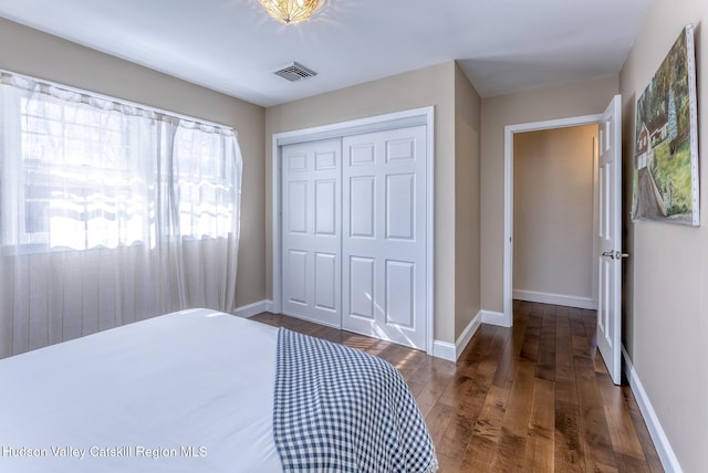 bedroom with a closet, dark wood-style flooring, visible vents, and baseboards