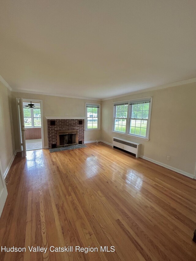 969 Blue Mountain Rd, Saugerties, NY 12477 - unfurnished living room featuring ornamental molding, light wood-type flooring, a brick fireplace, and radiator
