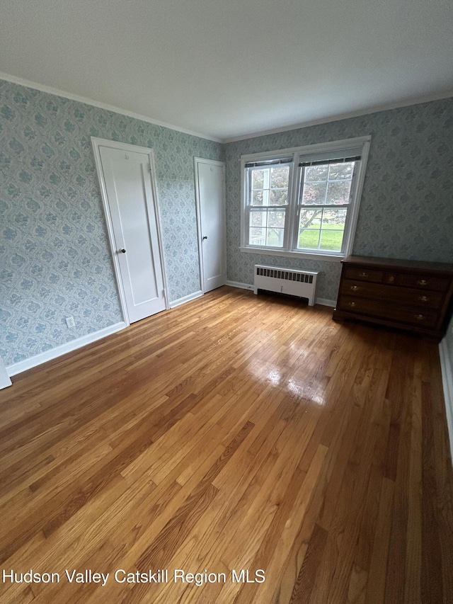 969 Blue Mountain Rd, Saugerties, NY 12477 - unfurnished bedroom featuring wallpapered walls, wood finished floors, ornamental molding, radiator, and multiple closets