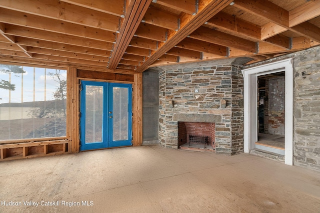 unfurnished living room with a stone fireplace and french doors