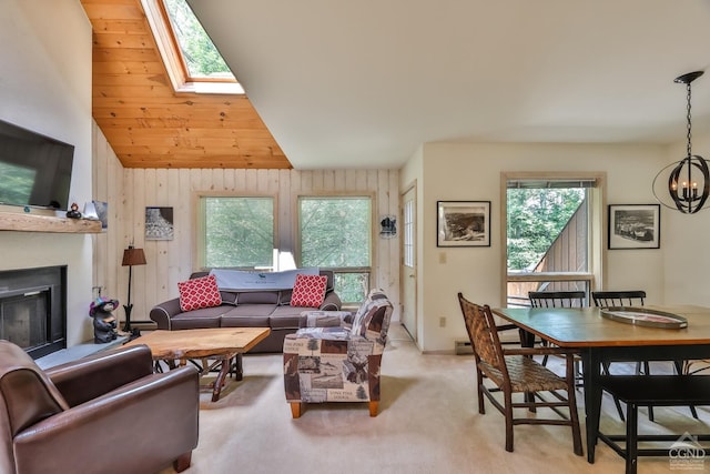 living area with plenty of natural light, a chandelier, a glass covered fireplace, light carpet, and vaulted ceiling