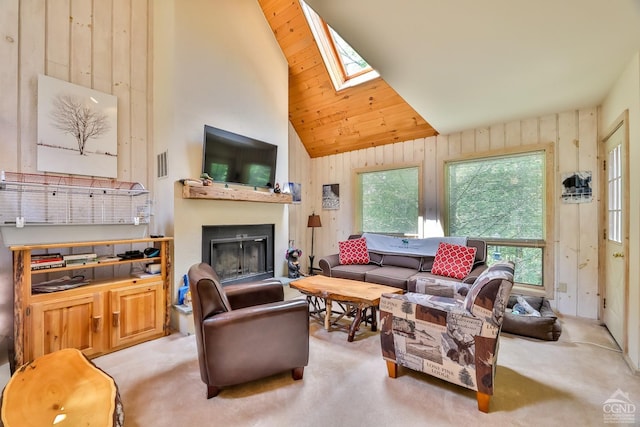 living room with a skylight, high vaulted ceiling, carpet floors, a glass covered fireplace, and wood walls