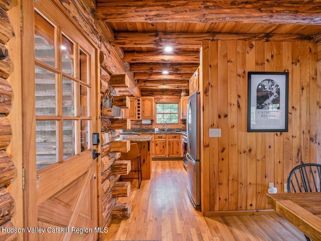 kitchen featuring wood walls, wood ceiling, stainless steel refrigerator, and light hardwood / wood-style flooring