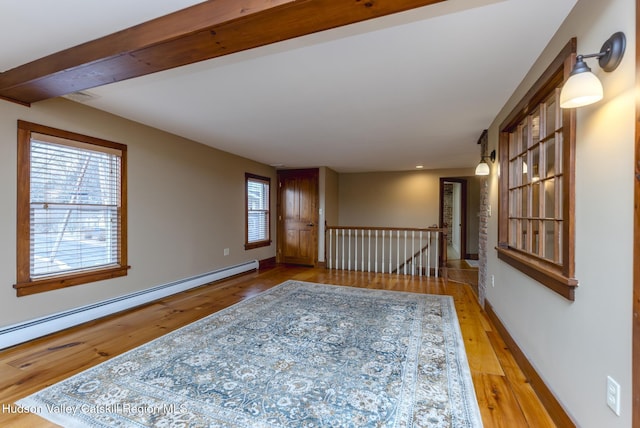 empty room with baseboard heating, light wood-type flooring, and a healthy amount of sunlight