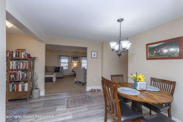 dining room with hardwood / wood-style floors, a baseboard heating unit, and a chandelier